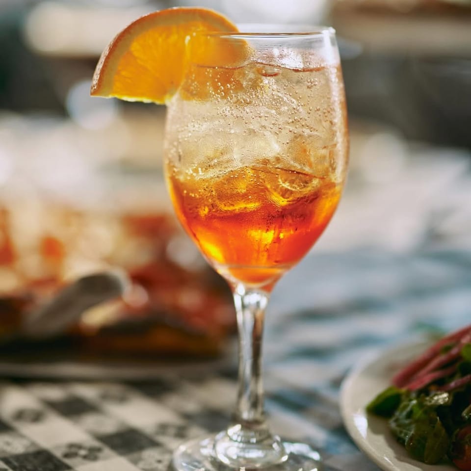 A refreshing orange cocktail with ice and an orange slice on a checkered tablecloth.