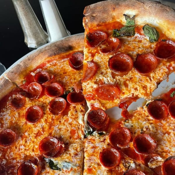 Close-up of a Charred Brick Oven pepperoni pizza with a slice removed, showing melted cheese and basil.