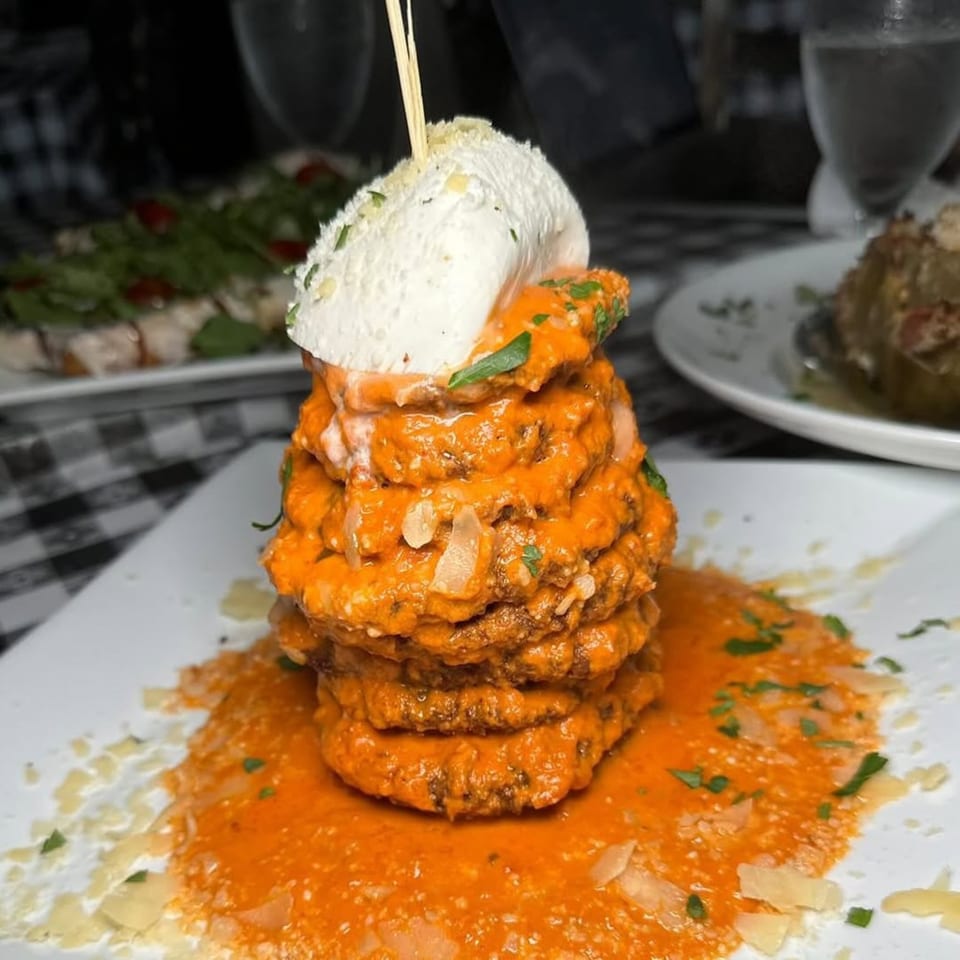 Stacked eggplant parmesan with red sauce and fresh mozzarella, garnished with herbs and cheese.