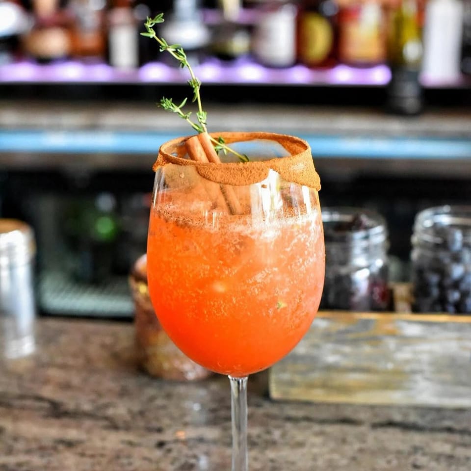 Orange cocktail with cinnamon sugar rim, cinnamon sticks, and thyme sprig at Charred Brick Oven.