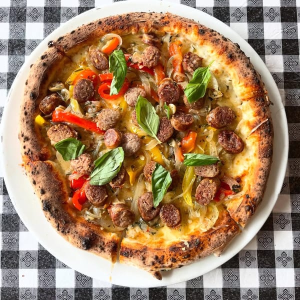 Charred Brick Oven pizza with sausage, peppers, onions, and fresh basil on a white plate.